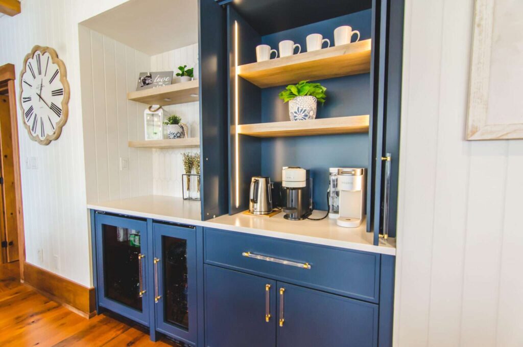 Navy blue built-in offee bar with brass hardware, LED shelf lighting, and natural wood shelf with white mugs