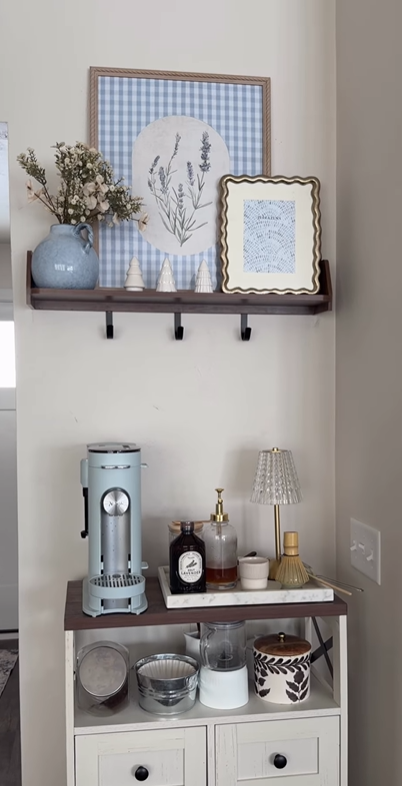 Small coffee bar with light blue espresso machine, gingham artwork, and wooden shelving